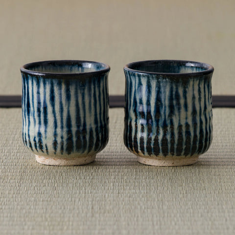 Two blue-and-white vertically striped teacups standing side by side on a tatami mat.