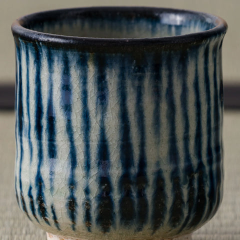 Tall cylindrical teacup with blue vertical brushstroke stripes on white and a dark blue rim, close view.