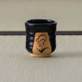 Black Kuro-Oribe yunomi with a lily of the valley motif brush-painted on an unglazed clay panel.