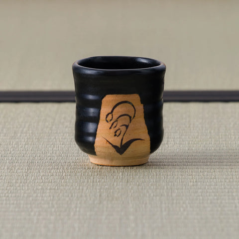 Black Kuro-Oribe yunomi with a lily of the valley motif brush-painted on an unglazed clay panel.
