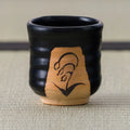 Close-up front view of the lily of the valley brushwork on a ribbed black Kuro-Oribe yunomi.