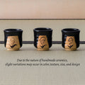 Three black lily of the valley yunomi in a row, with a note that handmade ceramics vary slightly.