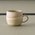 Beige stoneware mug with horizontal brushed-slip striping and a loop handle, front view on tatami