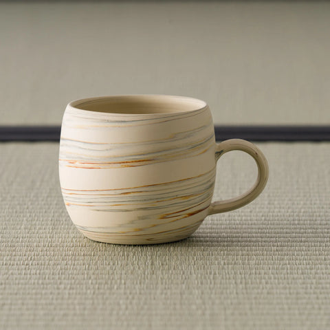 Beige stoneware mug with horizontal brushed-slip striping and a loop handle, front view on tatami