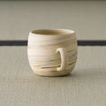 Side view of the beige mug showing the horizontal banded pattern and curved handle