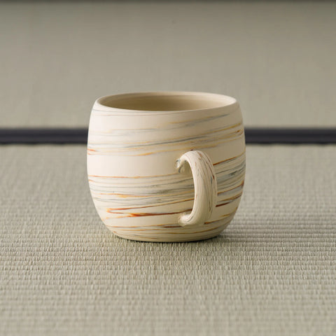 Side view of the beige mug showing the horizontal banded pattern and curved handle