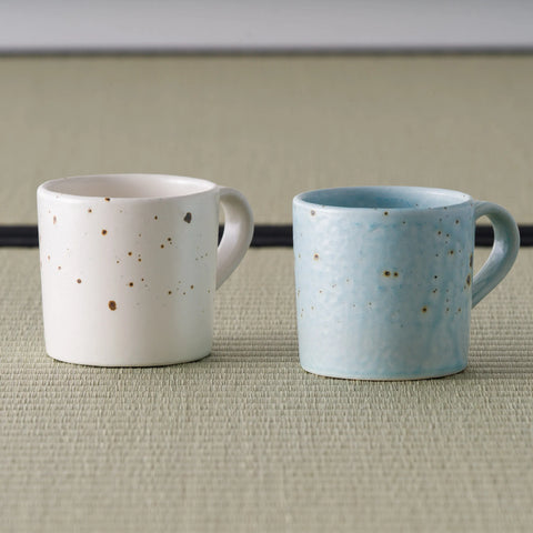 Two speckled mugs shown together for comparison, one in pale pink and one in blue-grey