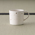 Pale pink speckled stoneware mug with a loop handle, front view on tatami