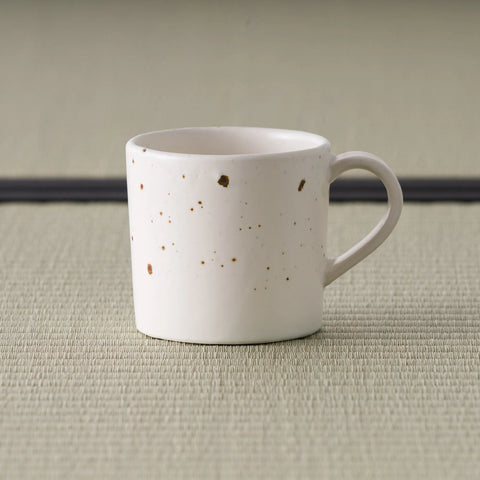 Pale pink speckled stoneware mug with a loop handle, front view on tatami