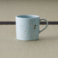 Pale blue-grey speckled stoneware mug with a loop handle, front view on tatami