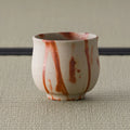 Three-quarter view of the yunomi showing the red scorch marks across the pale surface