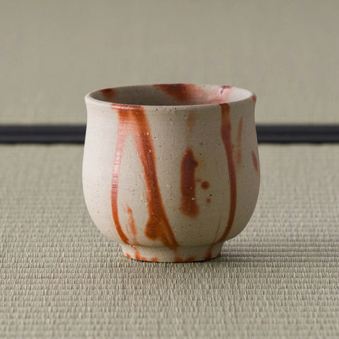 Three-quarter view of the yunomi showing the red scorch marks across the pale surface