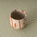 Cream-and-red yunomi tipped to show the foot and underside