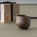 Wood-fired stoneware yunomi in earthy brown tones shown with its wooden storage box on tatami