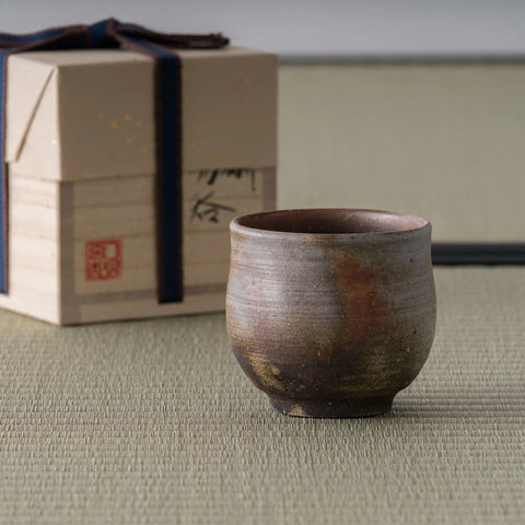 Wood-fired stoneware yunomi in earthy brown tones shown with its wooden storage box on tatami