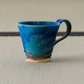Teal-blue glazed mug with a handle, side view on a tatami mat.