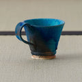 Teal-blue glazed mug with a handle and unglazed foot, side view on a tatami mat.