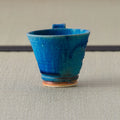 Tall deep blue glazed cup with a small lug handle, viewed showing the interior, on a tatami mat.