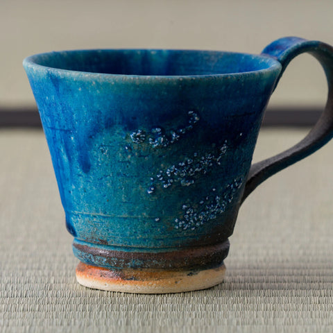 Teal-blue glazed mug with a handle, side view on a tatami mat.