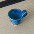 Blue glazed mug with a handle, viewed from above showing the interior, on a tatami mat.