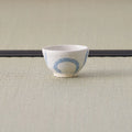 Small white cup with a blue design tipped over to show its base, on a tatami mat.