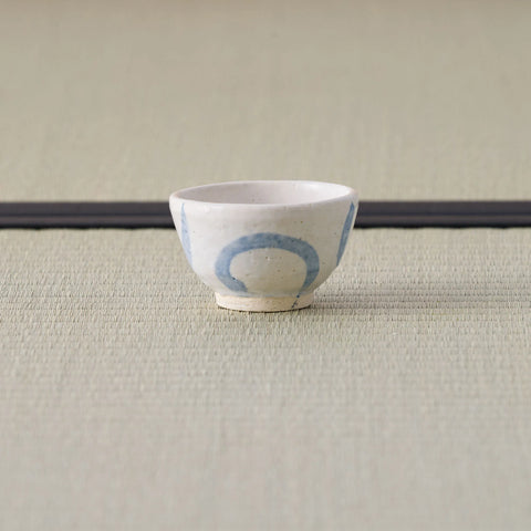 Small white cup with a blue design tipped over to show its base, on a tatami mat.