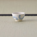 Small white cup with a blue arc design, side view on a tatami mat.