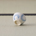 Small white cup with blue arcs tipped over to show its base, on a tatami mat.
