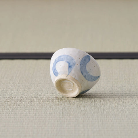 Small white cup with blue arcs tipped over to show its base, on a tatami mat.