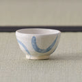 Small white cup with blue crescent brushwork, side view on a tatami mat.