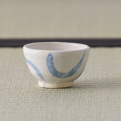 Small white cup with blue crescent brushwork, side view on a tatami mat.