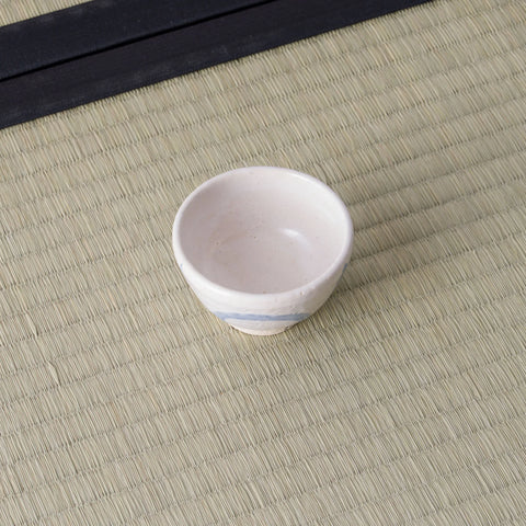 Small white cup with pale blue rings, front view on a tatami mat.