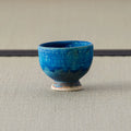 Deep teal-blue glazed footed cup, side view on a tatami mat.