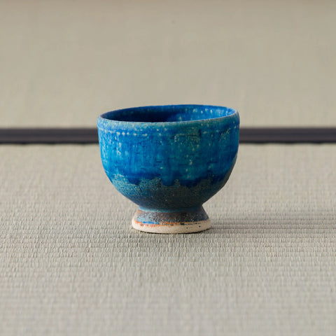 Deep teal-blue glazed footed cup, side view on a tatami mat.