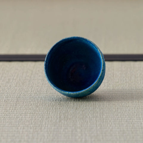 Deep blue glazed cup viewed at an angle showing the interior, on a tatami mat.