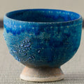 Deep blue glazed footed tea bowl, close side view on a tatami mat.