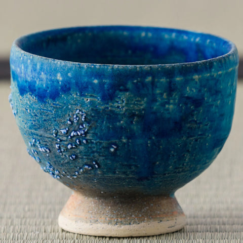Deep blue glazed footed tea bowl, close side view on a tatami mat.