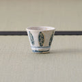 White cup with a blue leaf-and-floral brush design, front view on a tatami mat.