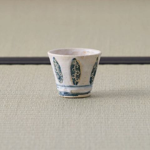 White cup with a blue leaf-and-floral brush design, front view on a tatami mat.