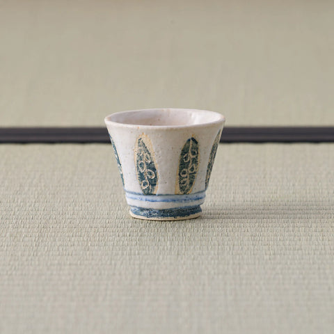 White cup with a blue leaf design, front view on a tatami mat.