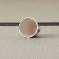 White cup with a blue design tipped over to show its interior, on a tatami mat.