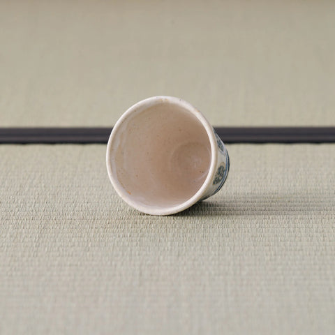 White cup with a blue design tipped over to show its interior, on a tatami mat.
