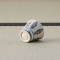 White cup with a blue leaf design tipped over to show its base, on a tatami mat.