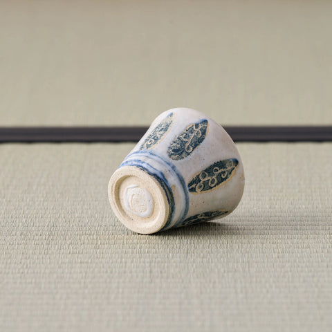 White cup with a blue leaf design tipped over to show its base, on a tatami mat.