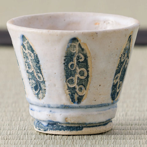 White cup with a blue leaf-and-oval design, front view on a tatami mat.
