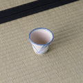 Small sandy stoneware cup with a blue triangle pattern, front view on a tatami mat.