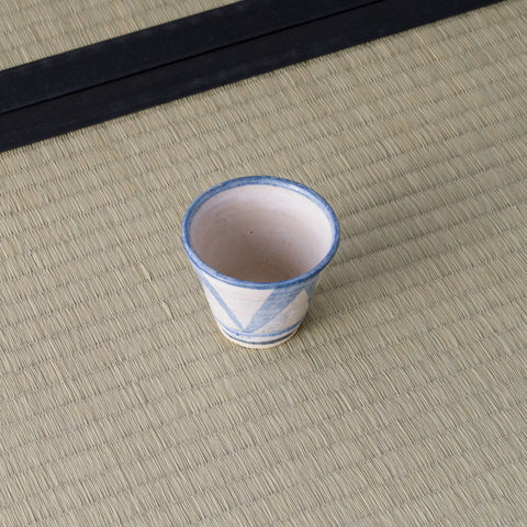 Small sandy stoneware cup with a blue triangle pattern, front view on a tatami mat.