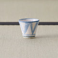 Sandy stoneware cup with a blue triangle pattern, front view on a tatami mat.