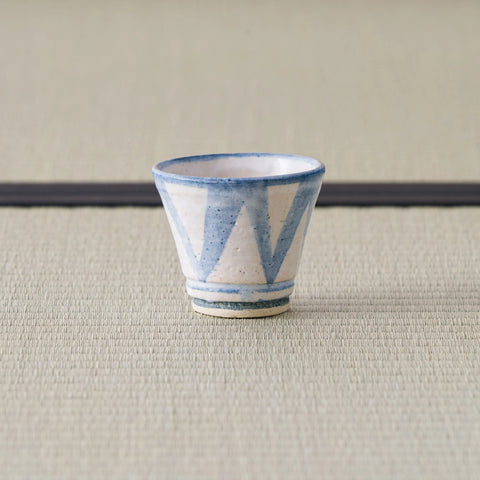 Sandy stoneware cup with a blue triangle pattern, front view on a tatami mat.
