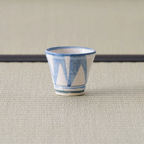 Sandy stoneware cup with a blue triangle pattern, front view on a tatami mat.
